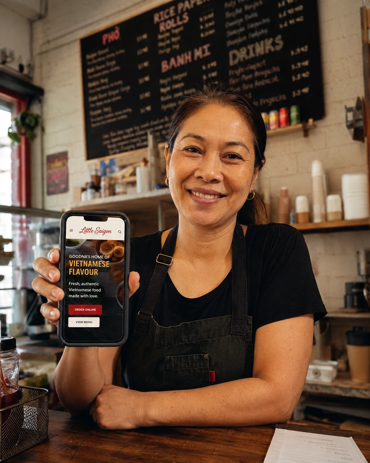 A cafe owner holding a phone showing a mobile website for a local Vietnamese restaurant.